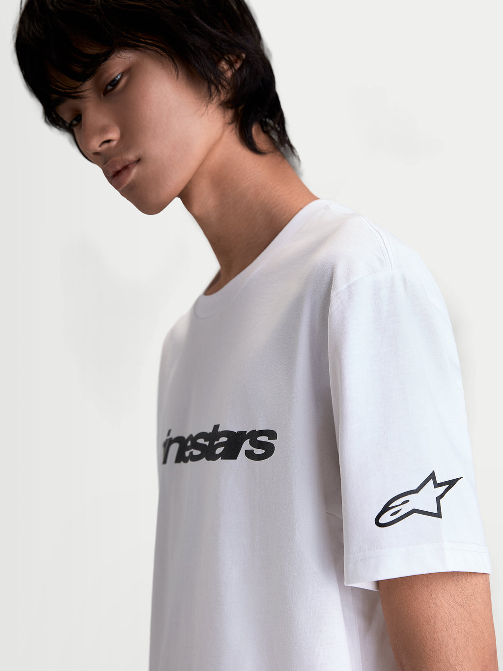 Alpinestars Race Wordmark CSF T-Shirt, hvid og sort kortærmet T-shirt, vist på model fra siden med wordmark på fronten og Ageless-stjernelogo på ærmet, afslappet sportswear i motorsportsstil.