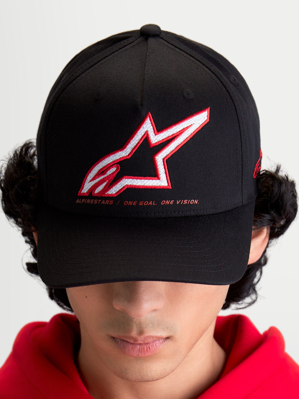 Alpinestars Lineout kasket, sportswear baseball-kasket til mænd og kvinder, sort med broderet rødt og hvidt Astars-logo og One Goal One Vision-slogan, buet skygge og struktureret krone, on-model, afslappet motorsport streetwear.