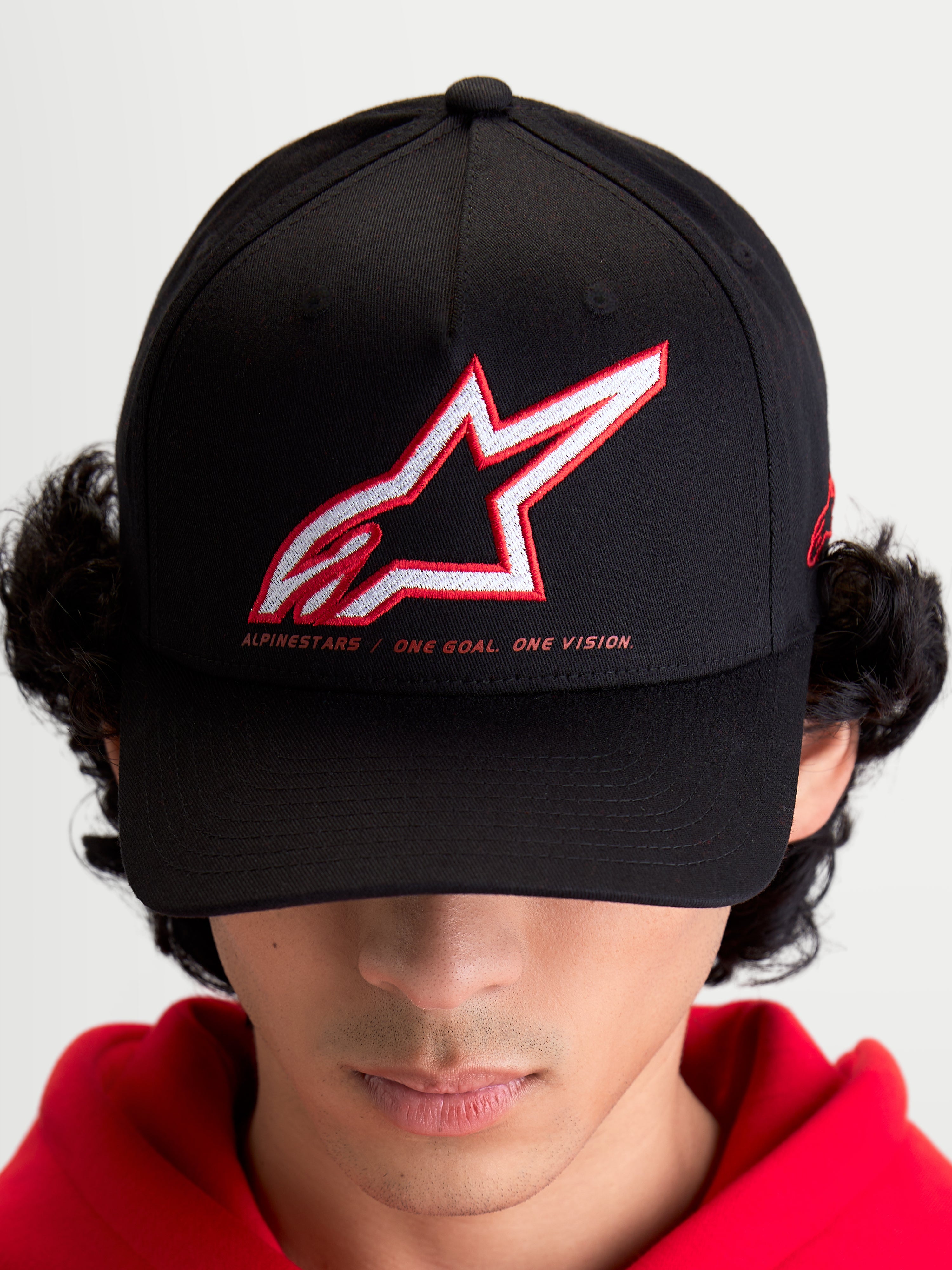 Alpinestars Lineout kasket, sportswear baseball-kasket til mænd og kvinder, sort med broderet rødt og hvidt Astars-logo og One Goal One Vision-slogan, buet skygge og struktureret krone, on-model, afslappet motorsport streetwear.