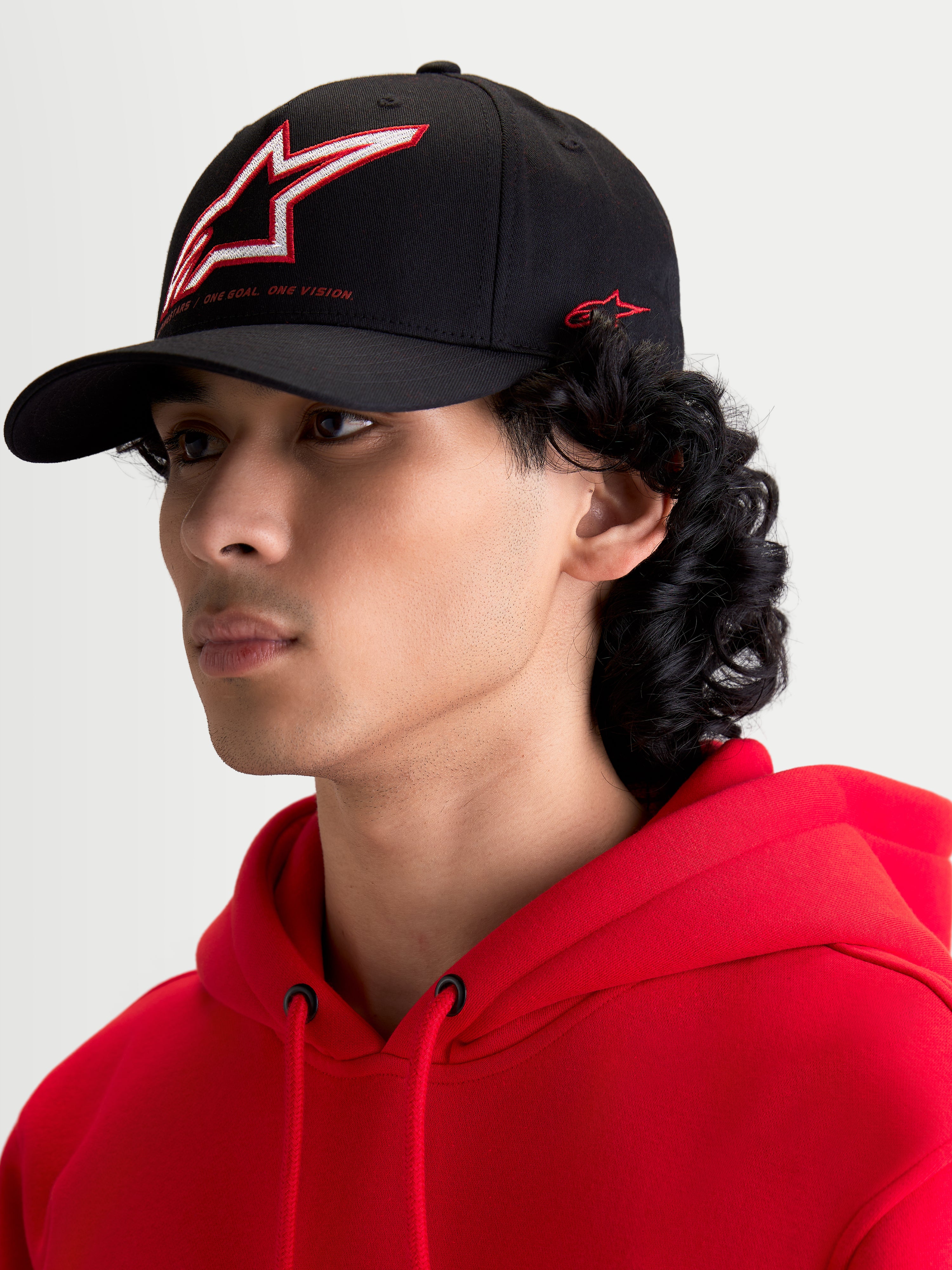 Alpinestars Lineout kasket, sort sportstøjskasket med buet skygge, struktureret krone med rød og hvidt broderet Astars-logo og sidebranding, vist på en model.