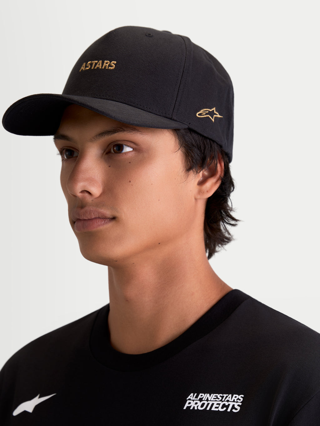 Alpinestars County Canvas kasket, sort sportswearkasket med guld ASTARS-ordlogo og guld broderet logo på siden, buet skygge og struktureret krone, peached oxford-stof, motorsport-inspireret til hverdagsbrug, vist på model.