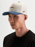 Alpinestars County Canvas Kasket, sportswear-kasket i sand og blå, båret af model, med buet skygge og broderet Astars-logo