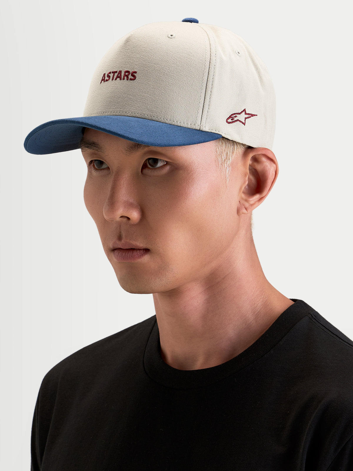 Alpinestars County Canvas Kasket, sportswear-kasket i sand og blå, båret af model, med buet skygge og broderet Astars-logo