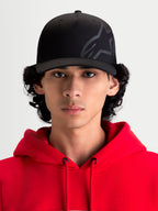 Alpinestars Maze kasket, sort motorsport-inspireret kasket, set forfra på model iført en rød hættetrøje. Har en struktureret krone, buet skygge og et tekstureret Astars Corp Shift-logo på slidstærkt twillstof til hverdagsbrug.