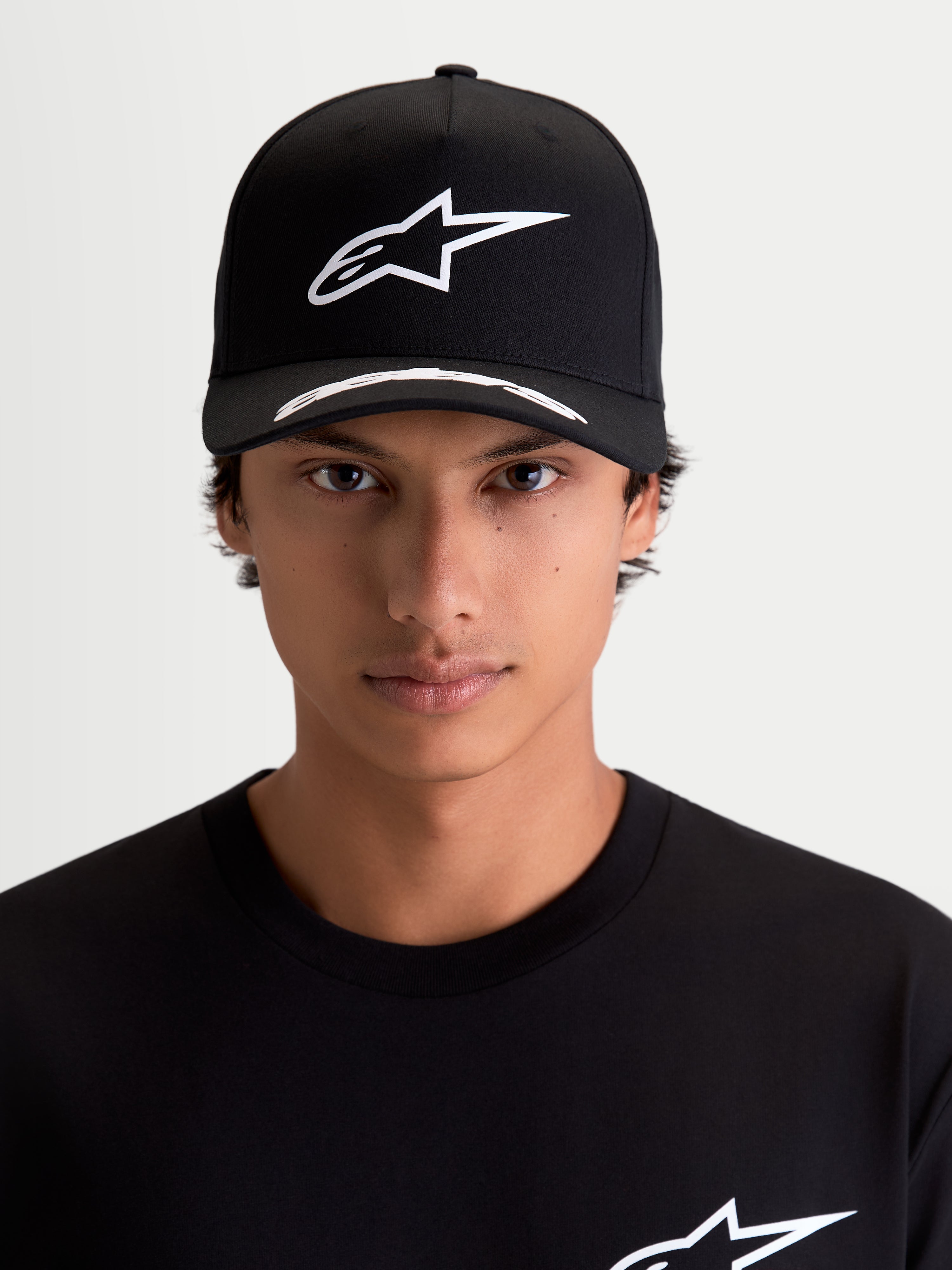 Alpinestars Arclight Hat, Black and White Motorsport Sportswear Cap, on-model front view. Features a white puff-print Astars logo on a structured crown, curved bill with logo detailing, and premium twill fabric.