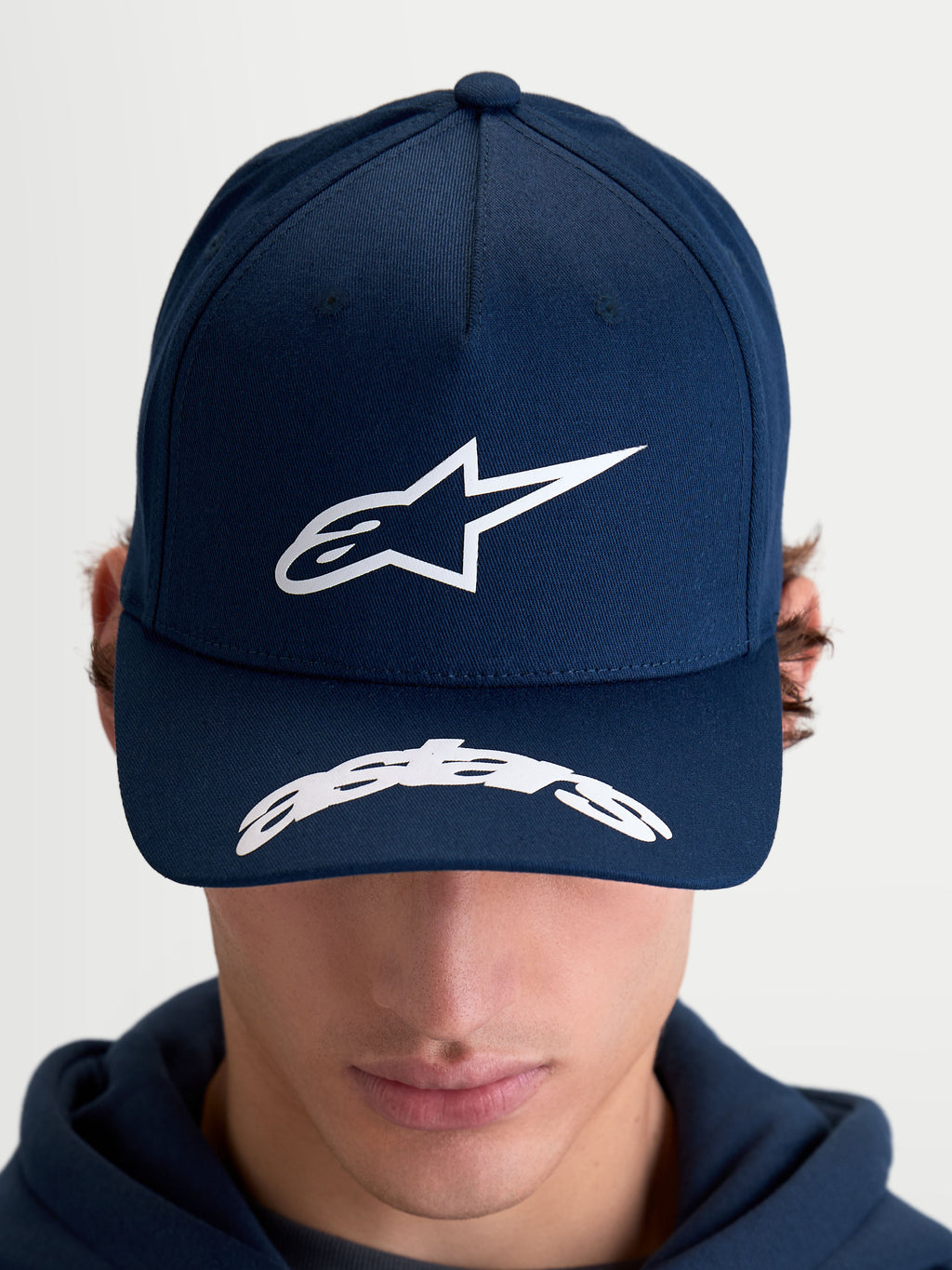 Alpinestars Arclight kasket, motorsportinspireret sportswear-kasket til herre og dame, mørkeblå og hvid, struktureret krone med tekstureret puff-print Astars-logo, buet skygge med Astars-detalje, slidstærk bomuldstwill, set forfra på model.