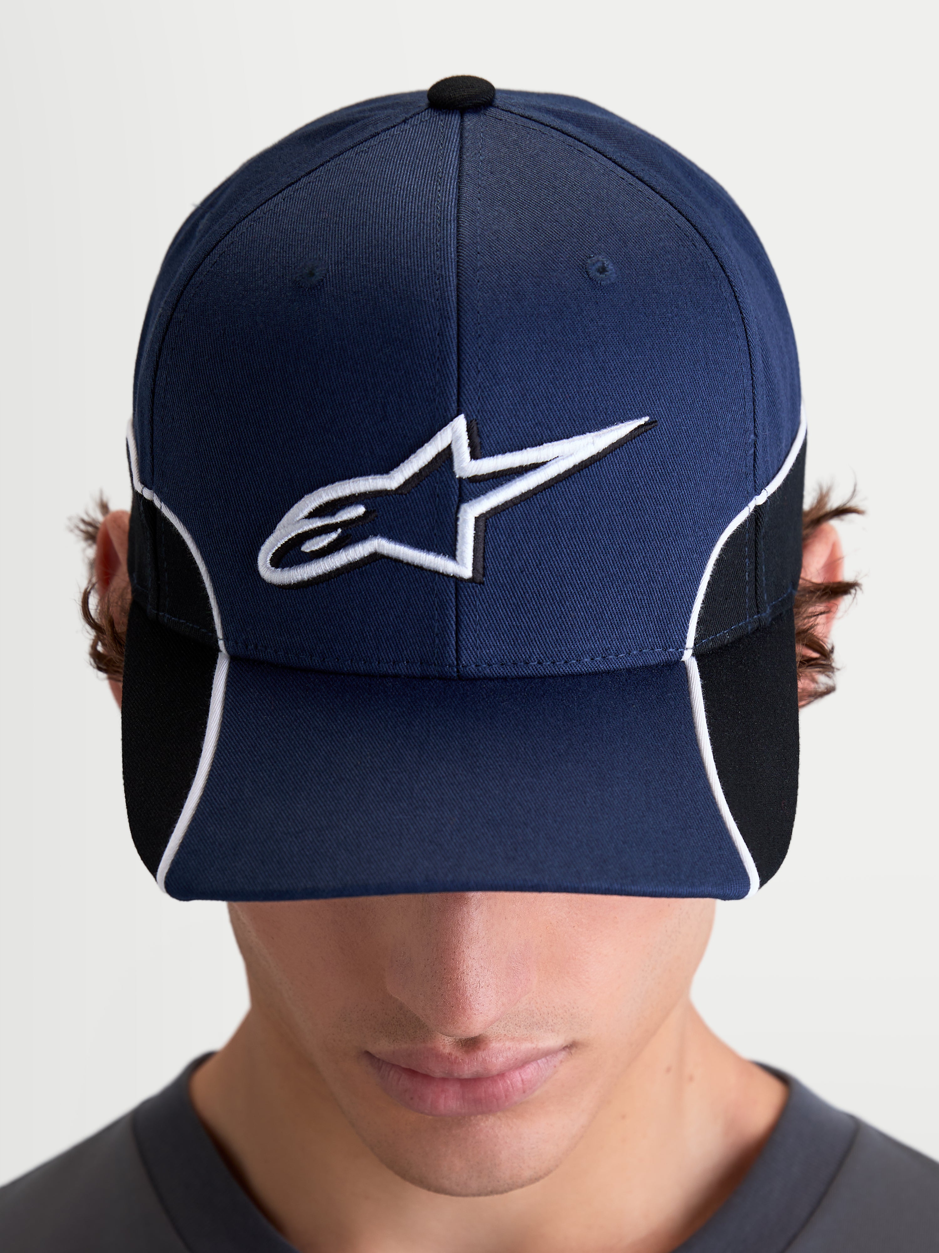 Alpinestars 500 Snapback Kasket, motorsport-inspireret sportswear-kasket, marineblå og sort, med buet skygge, 3D-broderet hvidt Astars-logo, hvid kontrastpiping og cut-and-sew-detaljer, set forfra på model.