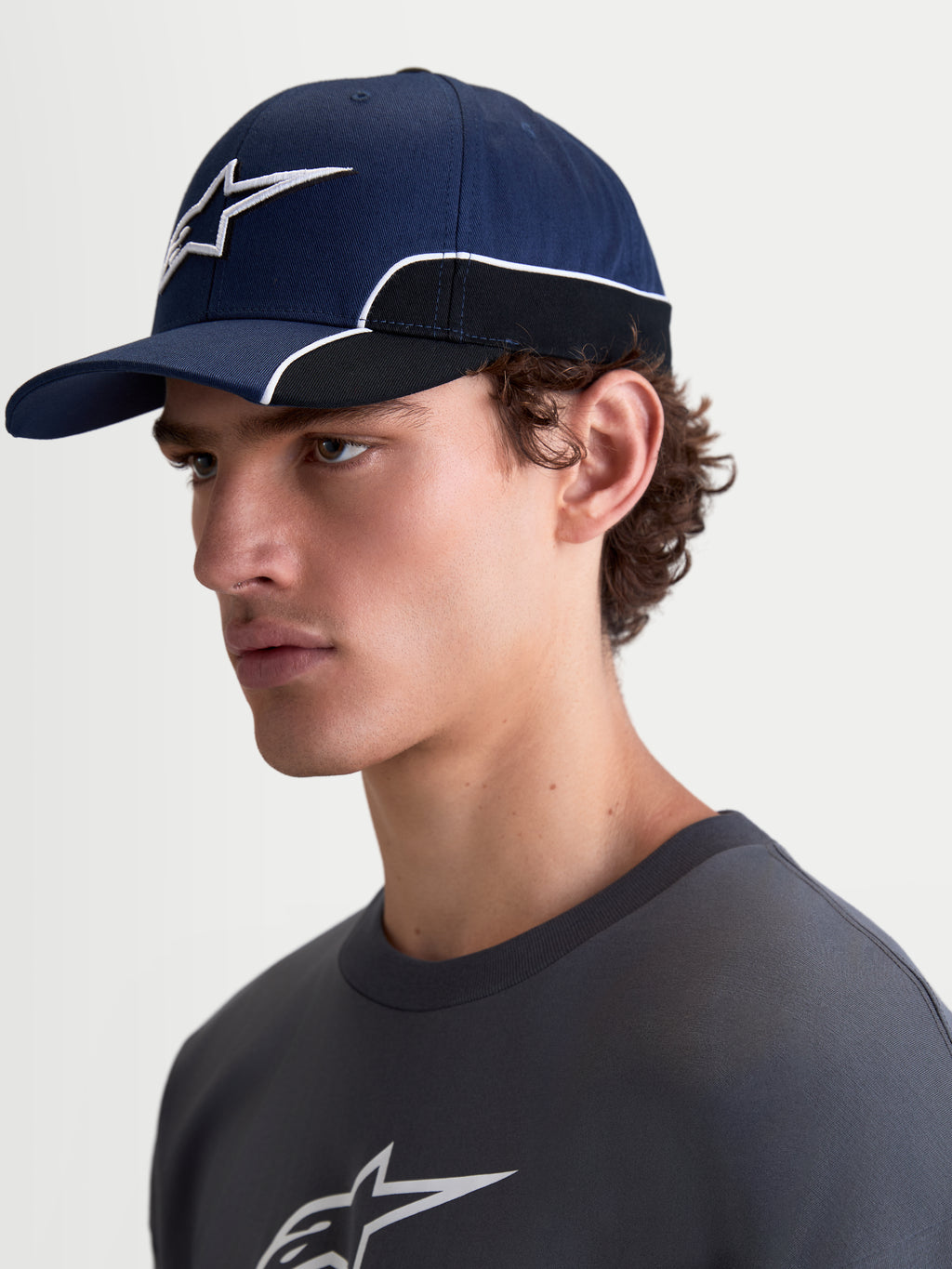 Alpinestars 500 Snapback kasket, sportswear baseball-kasket, unisex, marineblå og sort, slidstærk bomuldstwill, med buet skygge og 3D Astars-logo broderi med hvid kontrastpiping, set fra siden på en model.