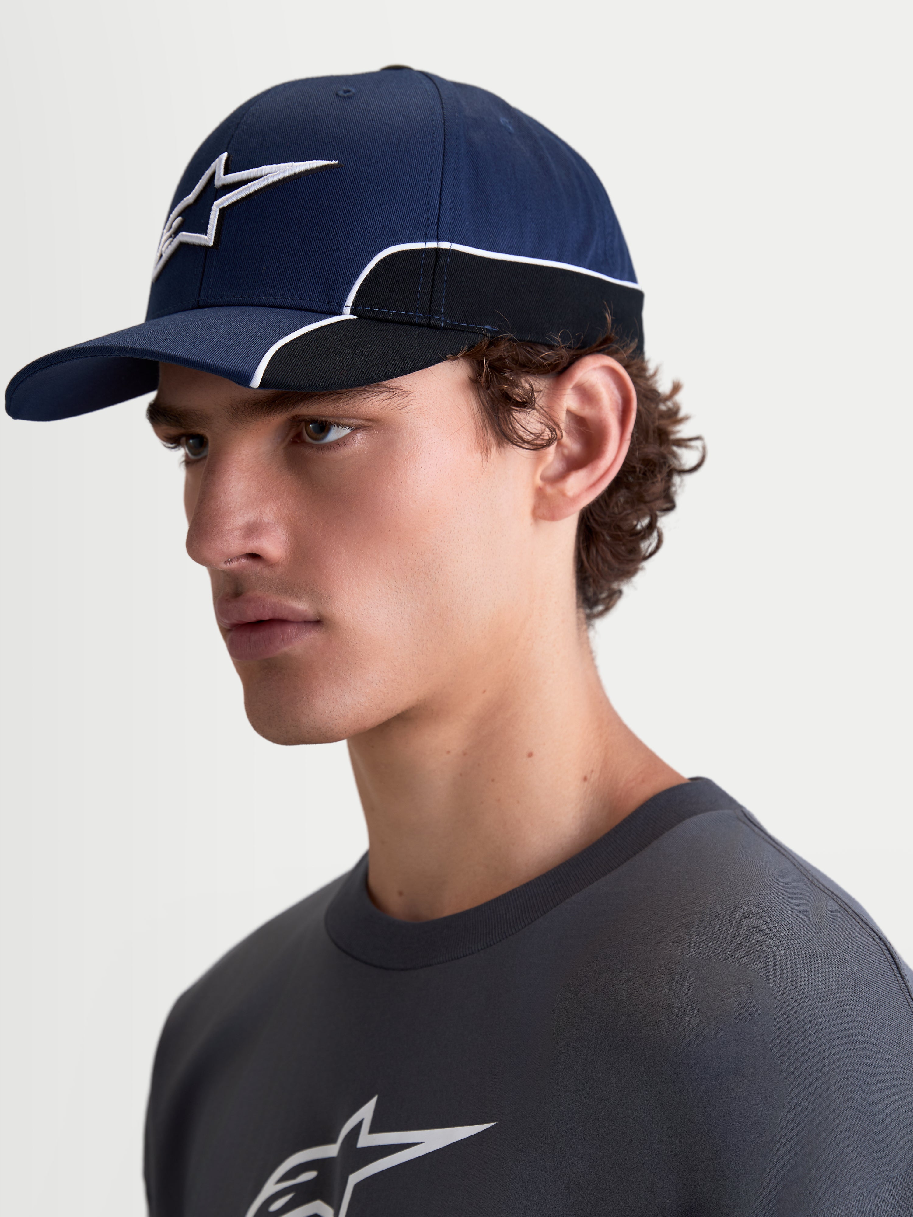 Alpinestars 500 Snapback kasket, sportswear baseball-kasket, unisex, marineblå og sort, slidstærk bomuldstwill, med buet skygge og 3D Astars-logo broderi med hvid kontrastpiping, set fra siden på en model.