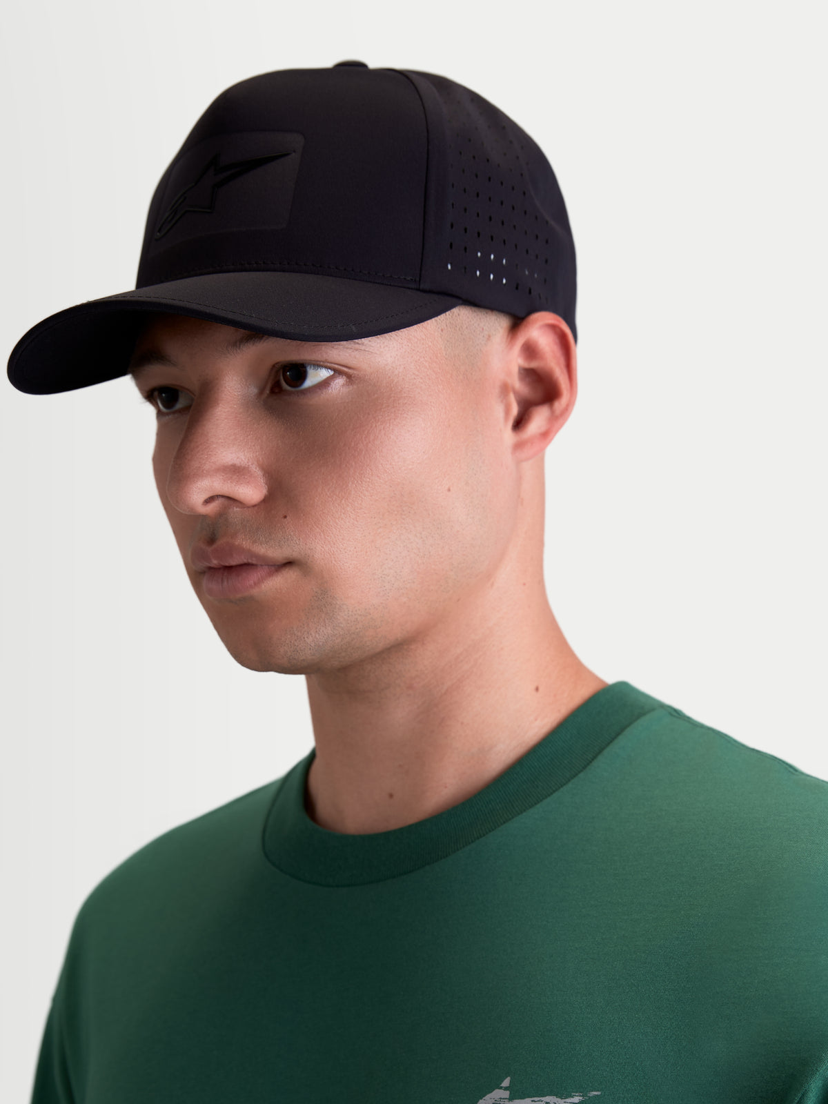 Alpinestars Algo Perf Ajustable Kasket, motorsportsinspireret sportswear kasket, sort, teknisk stof med sideperforering for ventilation, buet skygge og tonalt sonic-weld Astars-logo, vist på person.