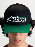 Alpinestars Retro Snapback Hat, Motorsport-inspired sportswear baseball cap with curved bill and structured crown, Unisex, Black and Green, Cotton Twill, front view on model showing the Astars logo with green pop-color running stitch detailing.