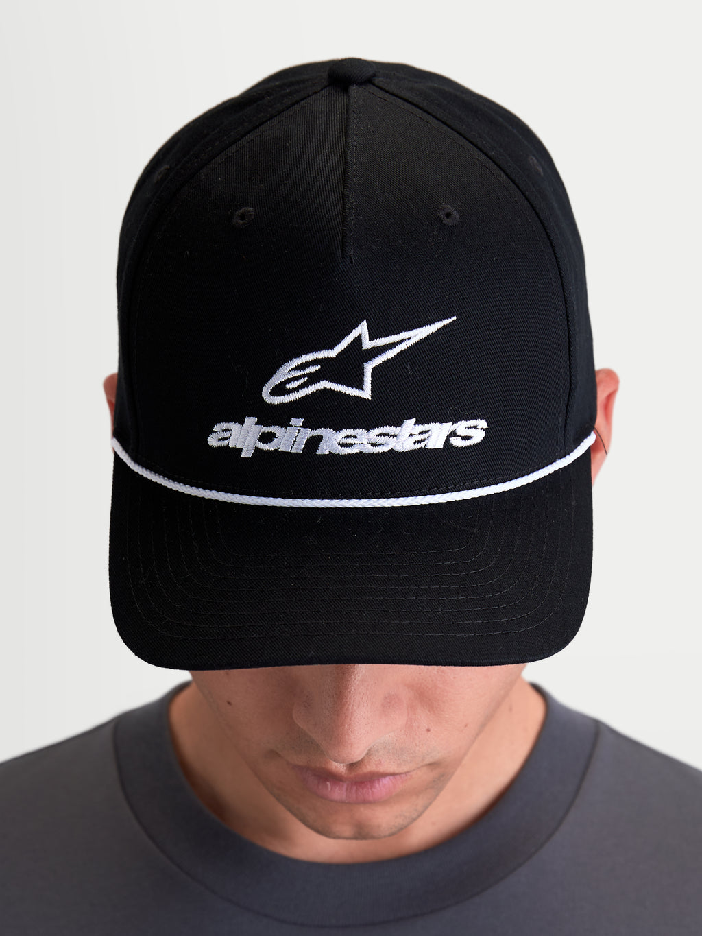 Alpinestars Combo Logo Snapback kasket, sort kasket vist på model med hvidt broderet Astars-logo og hvid dekorativ snor, struktureret krone og buet skygge, unisex afslappet sportswear til motorsport.
