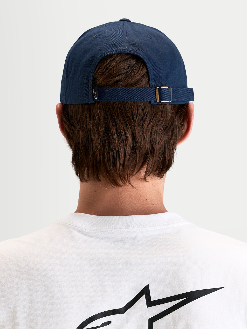 Alpinestars Dylan Dad Hat, casual sportswear cap in navy blue, rear view showing the adjustable strap-back closure with metal buckle and small Astars logo tag worn by a model
