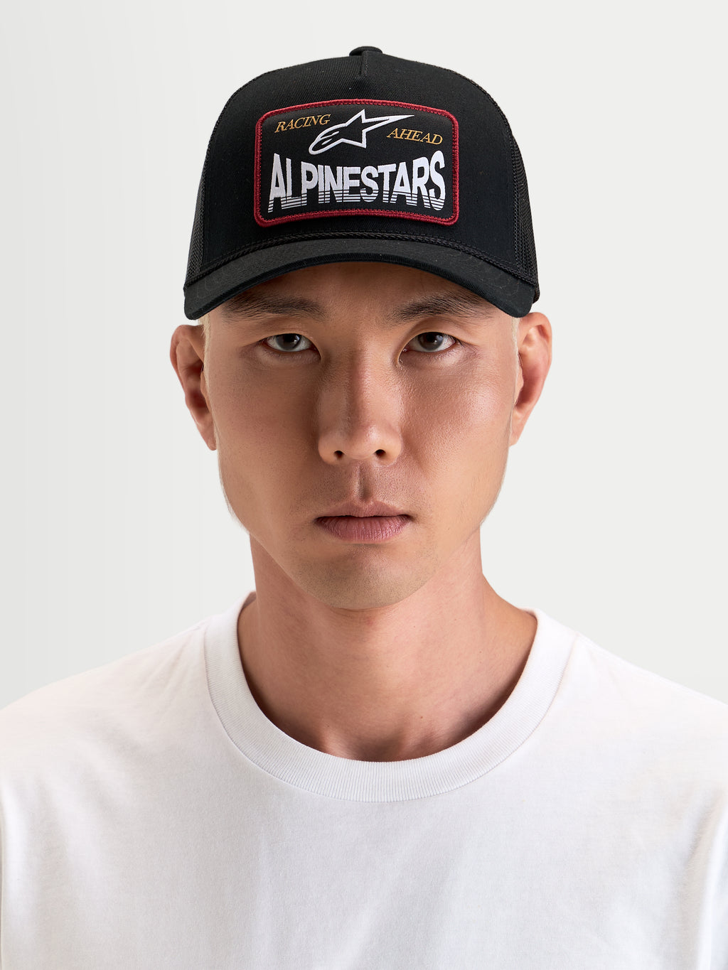 Alpinestars Hemmings Trucker Hat, black sportswear cap with curved bill and breathable mesh back, featuring a front Alpinestars word combo logo woven patch, worn by a model.