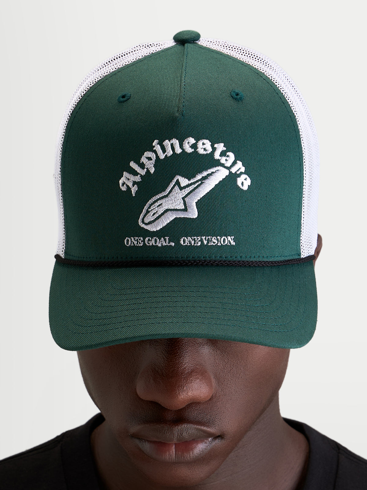 Alpinestars Baron Trucker Cap, grøn og hvid trucker cap med buet skygge, struktureret twill-front, åndbar poly mesh-bagside og broderet logo foran, båret af model