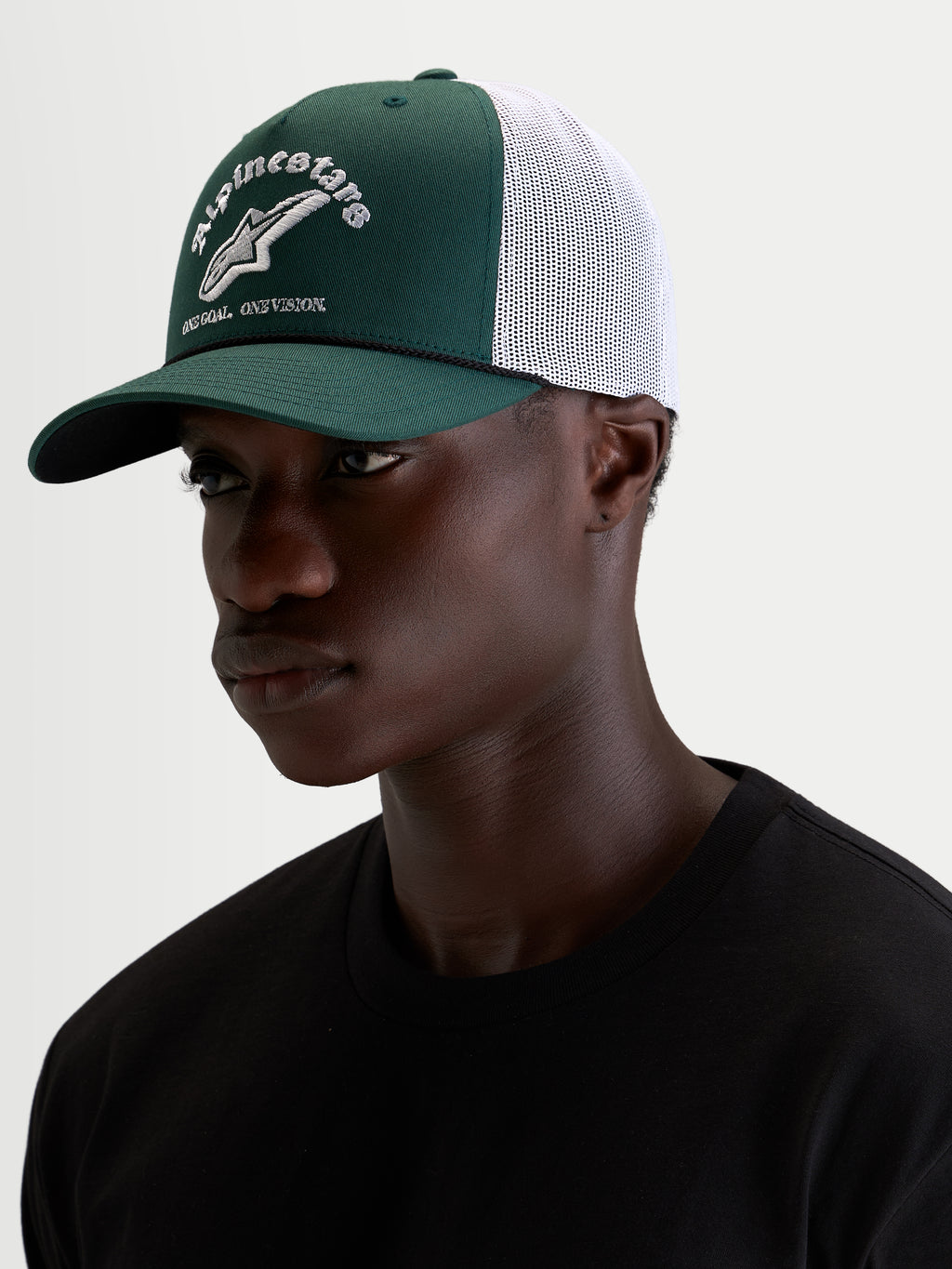 Alpinestars Baron Trucker Cap, grøn og hvid casual sportswear-kasket, båret af model med buet skygge, struktureret twill-krone og broderet logo foran