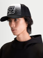 Alpinestars Gravel Trucker cap, afslappet kasket til sportstøj på model, sort og hvid, med struktureret krone, buet skygge og åndbar mesh-bagside. Forsiden har et vævet patch med grusstruktur-grafik og Alpinestars Racing Ahead-branding.