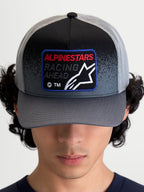 Alpinestars Gravel Trucker Cap, mørkegrå og sort truckerkasket, buet skygge og vævet frontpatch med 'Racing Ahead'-tekst og Astars-logo, vist på model set forfra.