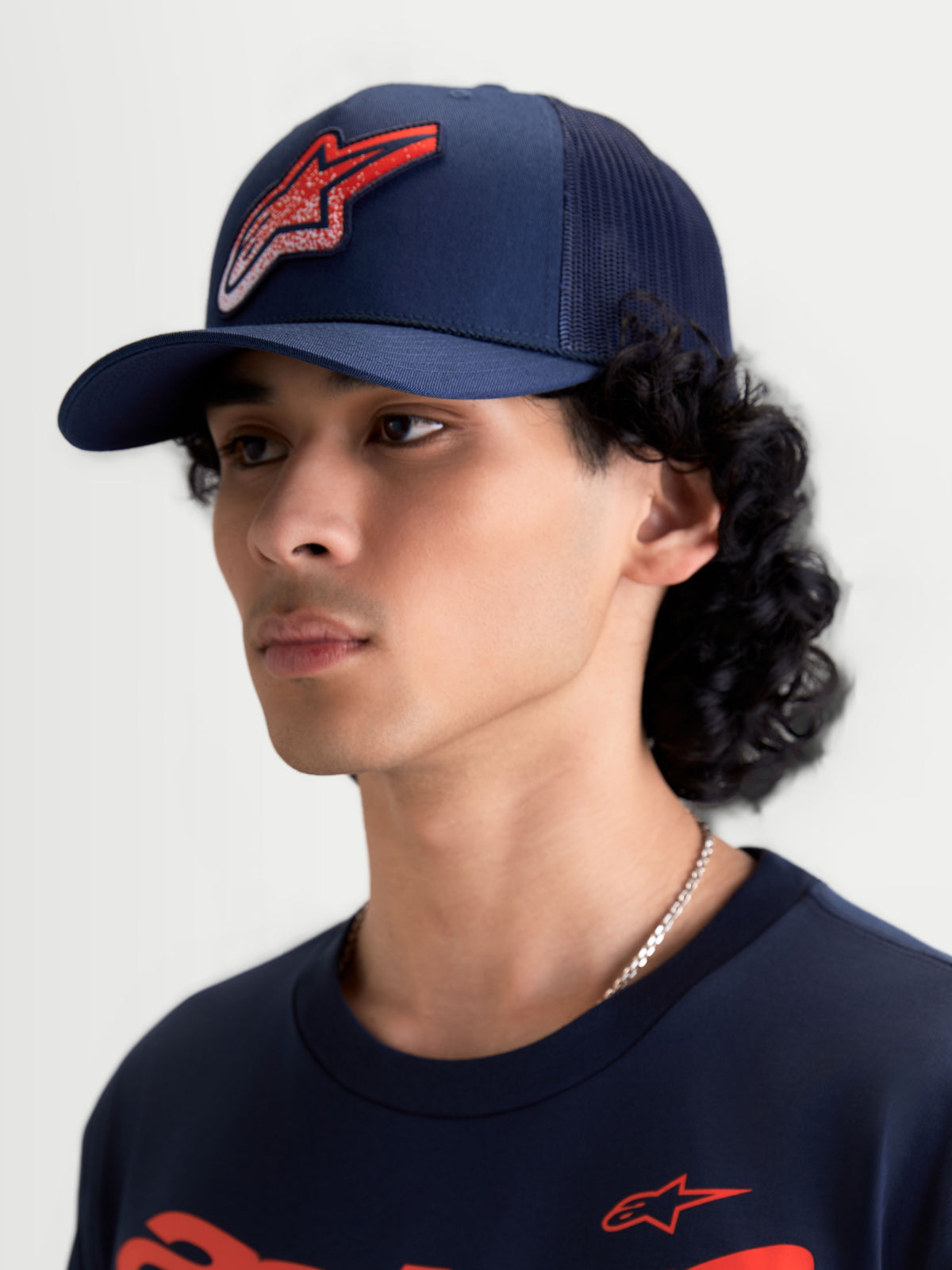 Alpinestars Meteorite Trucker cap, mørkeblå kasket med mesh-bagside og rødt Astars-logo med grustekstur, buet skygge og struktureret krone, vist på model, afslappet motorsport sportstøj