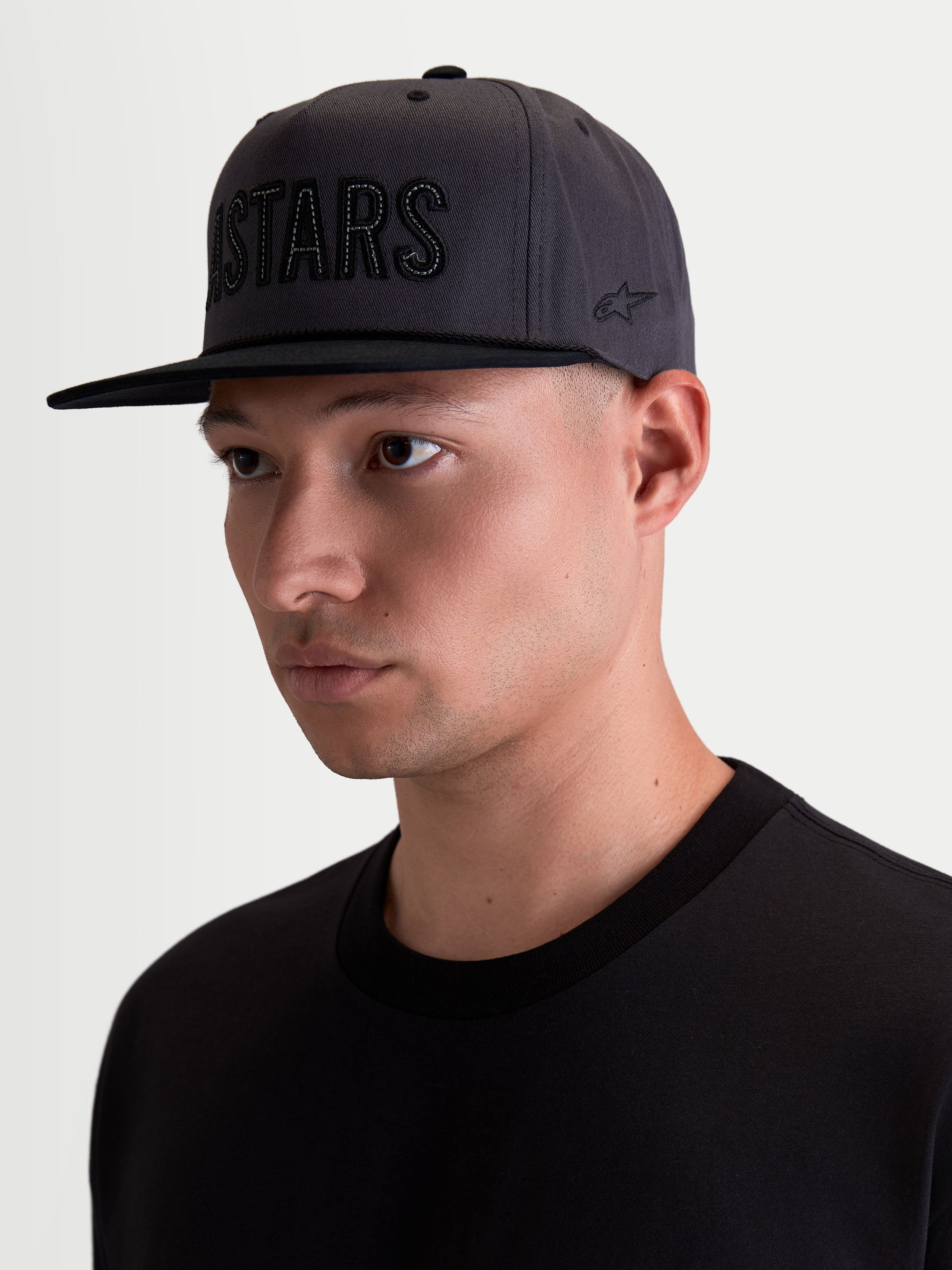 Alpinestars Stadium Snapback kasket, motorsport-inspireret herrekasket, mørkegrå og sort, struktureret krone med flad skygge, ASTARS-logoapplikation foran og broderet logo på siden, bomuldstwill, vist på model.