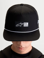 Alpinestars Label Snapback kasket, sportswear-kasket til hverdagsbrug, unisex, sort og hvid, bomuldstwill, med struktureret krone, flad skygge, hvid snøre og et vævet mærke foran med Alpinestars branding, vist på model.