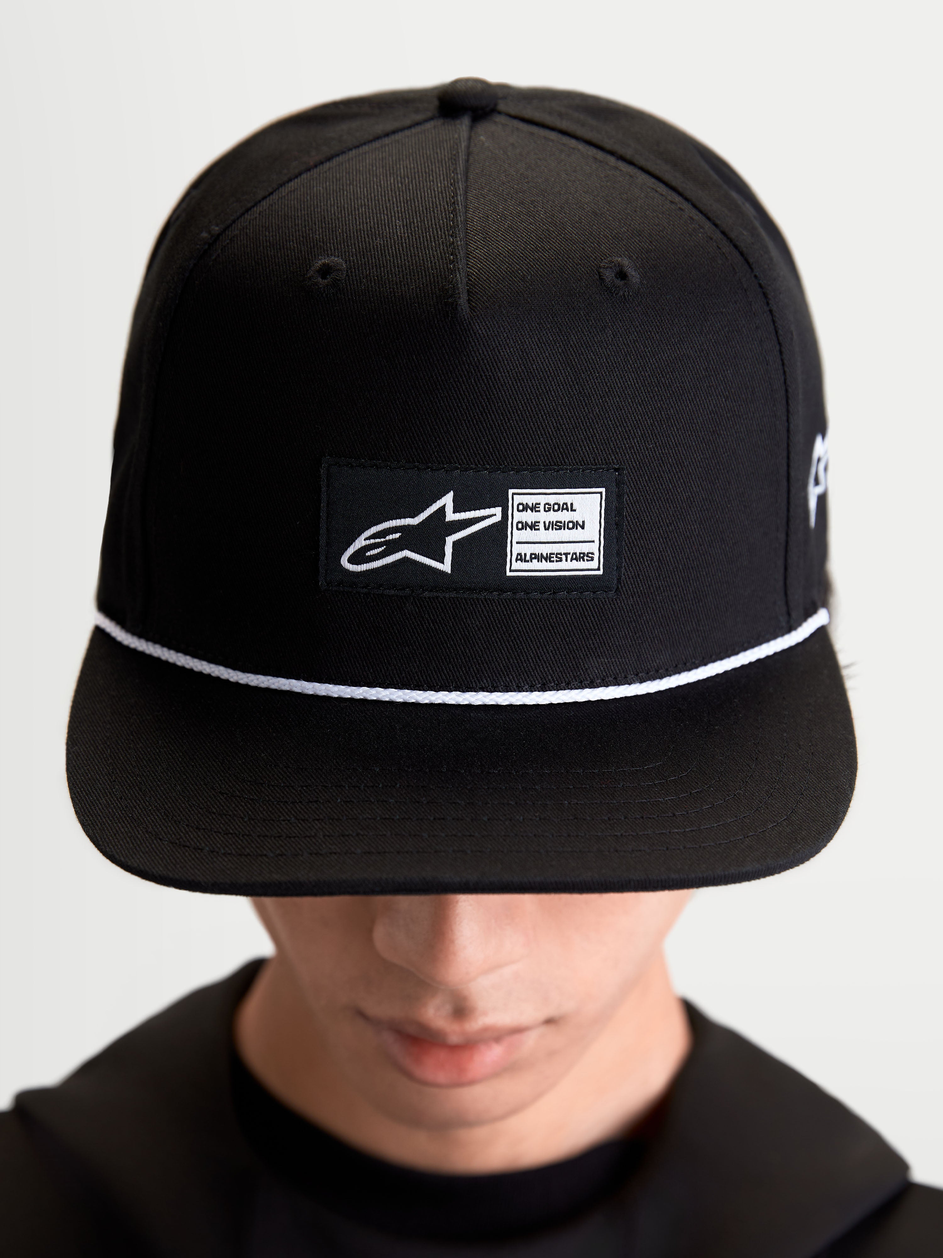 Alpinestars Label Snapback kasket, sportswear-kasket til hverdagsbrug, unisex, sort og hvid, bomuldstwill, med struktureret krone, flad skygge, hvid snøre og et vævet mærke foran med Alpinestars branding, vist på model.