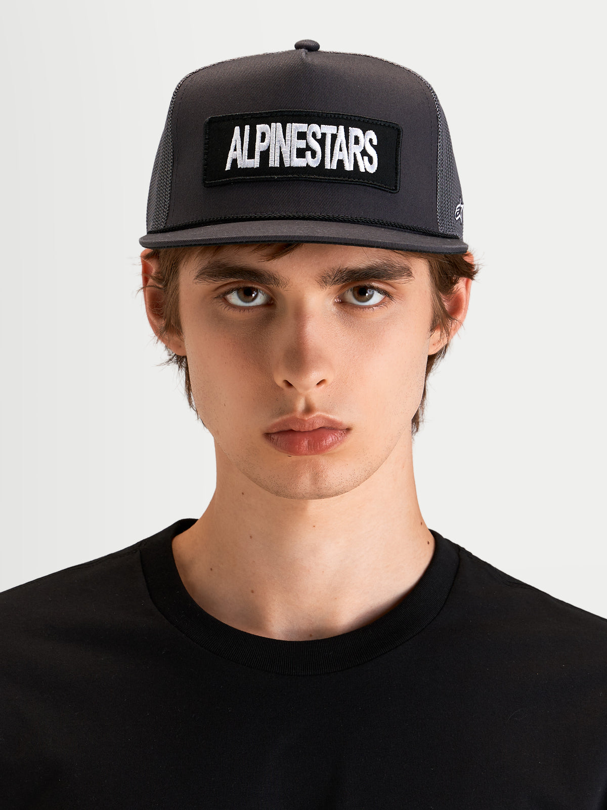 Alpinestars Ten Trucker Cap, mørkegrå sportswear-kasket med flad skygge, båret af model med struktureret krone og broderet Alpinestars-logo foran