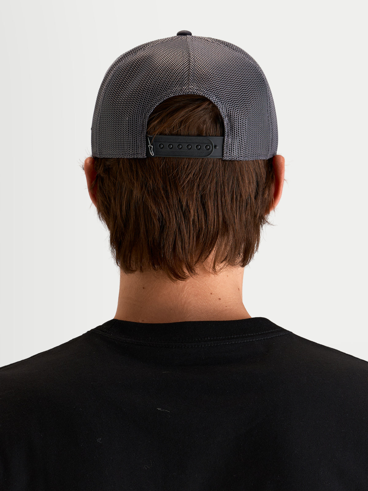 Alpinestars Ten Trucker Cap, mørkegrå kasket, set bagfra på en model der viser justerbar snapback-lukning, mesh-bagpaneler og mærkedetaljer bagpå