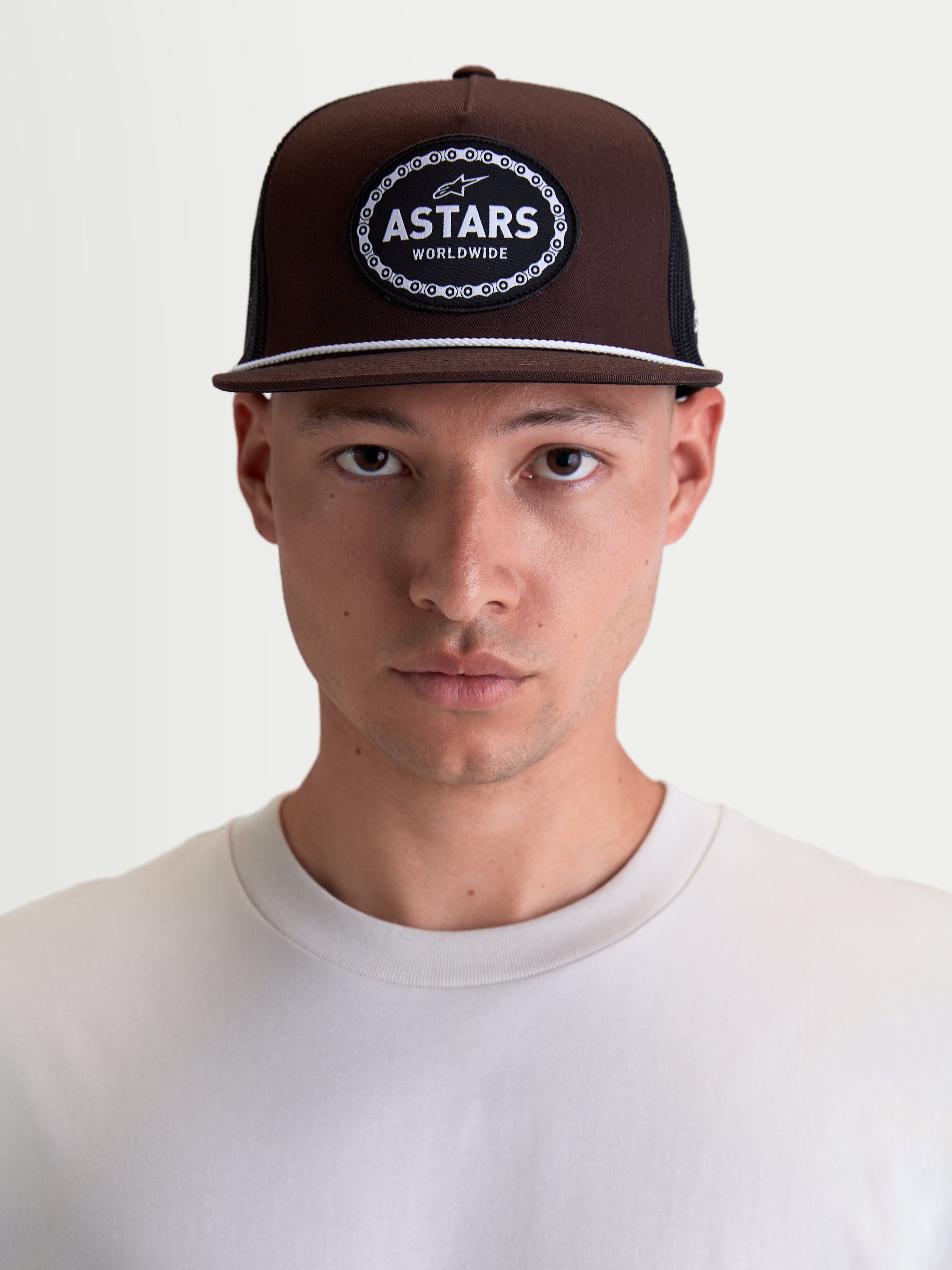 Alpinestars Hotlink Trucker cap, motorsportinspireret streetwear-kasket, brun og sort, struktureret krone og flad skygge med hvid snore-detalje, vævet Astars Worldwide-logomærke foran, vist på model.
