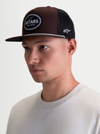 Alpinestars Hotlink Trucker kasket på model, brun og sort motorsport-inspireret kasket med flad skygge, struktureret twill-krone og vævet Astars-logomærke med cykelkædekant, casual streetwear