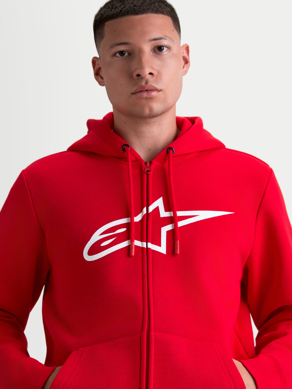 Alpinestars Ageless Zip V3 hættetrøje, rød sportswear-hættetrøje med gennemgående lynlås og hvidt A-star brystlogo, design med hætte og justerbare snore, vist på model for et motorsport-inspireret look.
