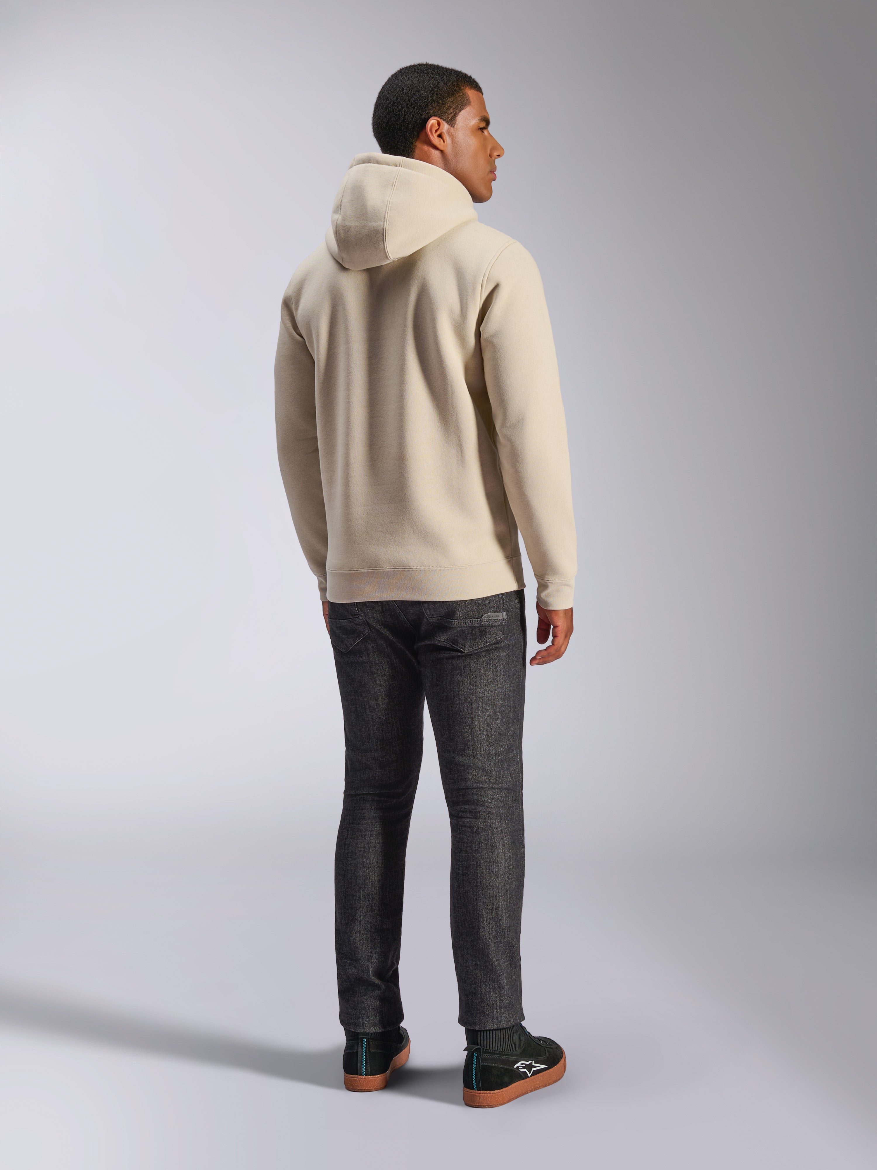 Alpinestars Ageless V3 Hoodie, casual off-white hooded pullover fleece shown from the back, features ribbed cuffs and hem, worn with dark slim-fit jeans and black Alpinestars sneakers
