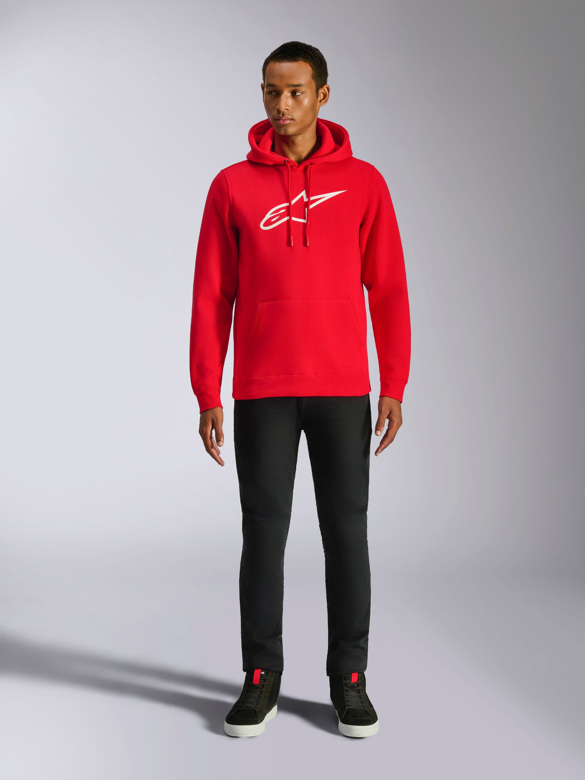 Alpinestars Ageless V3 hættetrøje, casual streetwear, rød med hvidt broderet Alpinestars-logo, båret af en mandlig model med sorte bukser, hætte med snoretræk, kængurulomme foran, moderne motorsport-inspireret design