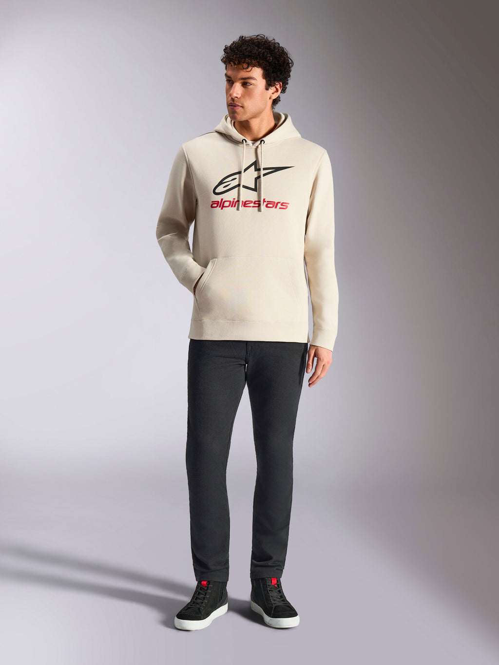 Alpinestars Always V3 hættetrøje, afslappet streetwear, råhvid med sort stjernelogo og rød skrift, hætte med snøre, lange ærmer, båret af mandlig model med sorte bukser og sorte sneakers