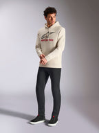 Alpinestars Always V3 Hoodie, råhvid pullover fleece-hættetrøje, lineært logo på fronten med sort stjerne og rød branding, båret af en mandlig model med sorte bukser og sorte sneakers, casual motorsport-streetwear