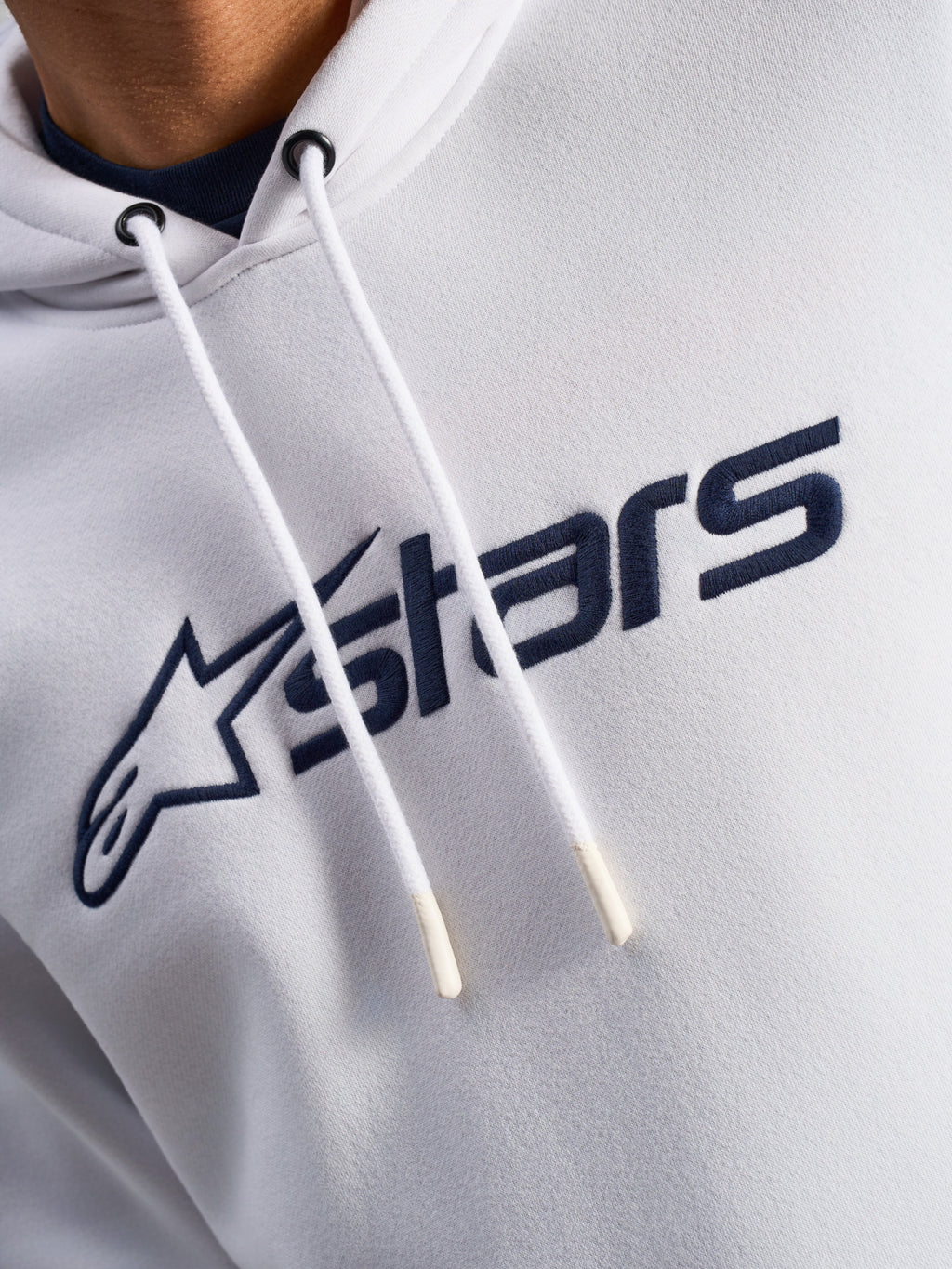 Alpinestars Blaze V3 hættetrøje, hvid og navyblå, nærbillede af brystet med navyblåt logoprint på fronten og hvide snore med dyppede spidser, afslappet motorsport-streetwear