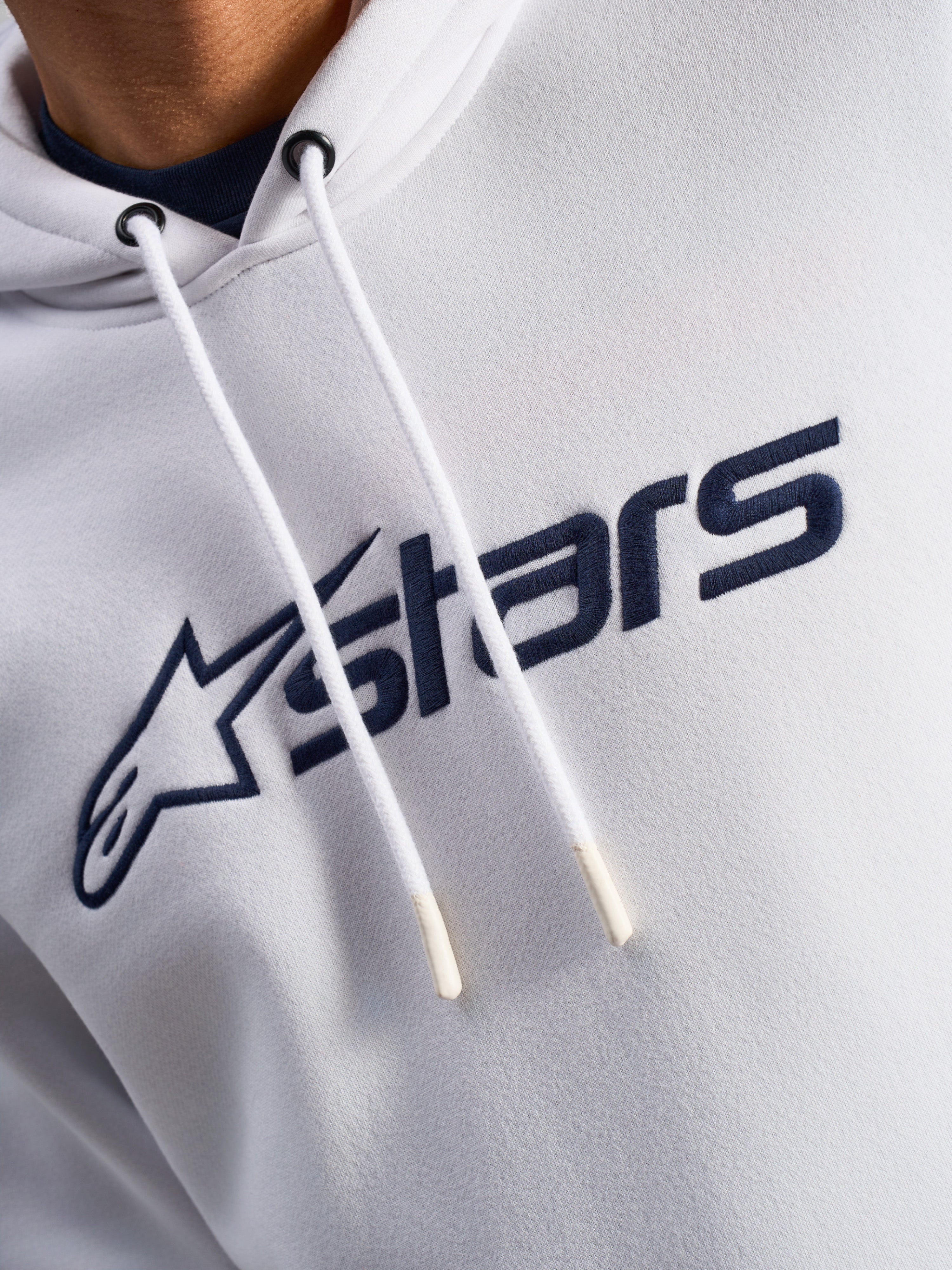 Alpinestars Blaze V3 hættetrøje, hvid og navyblå, nærbillede af brystet med navyblåt logoprint på fronten og hvide snore med dyppede spidser, afslappet motorsport-streetwear