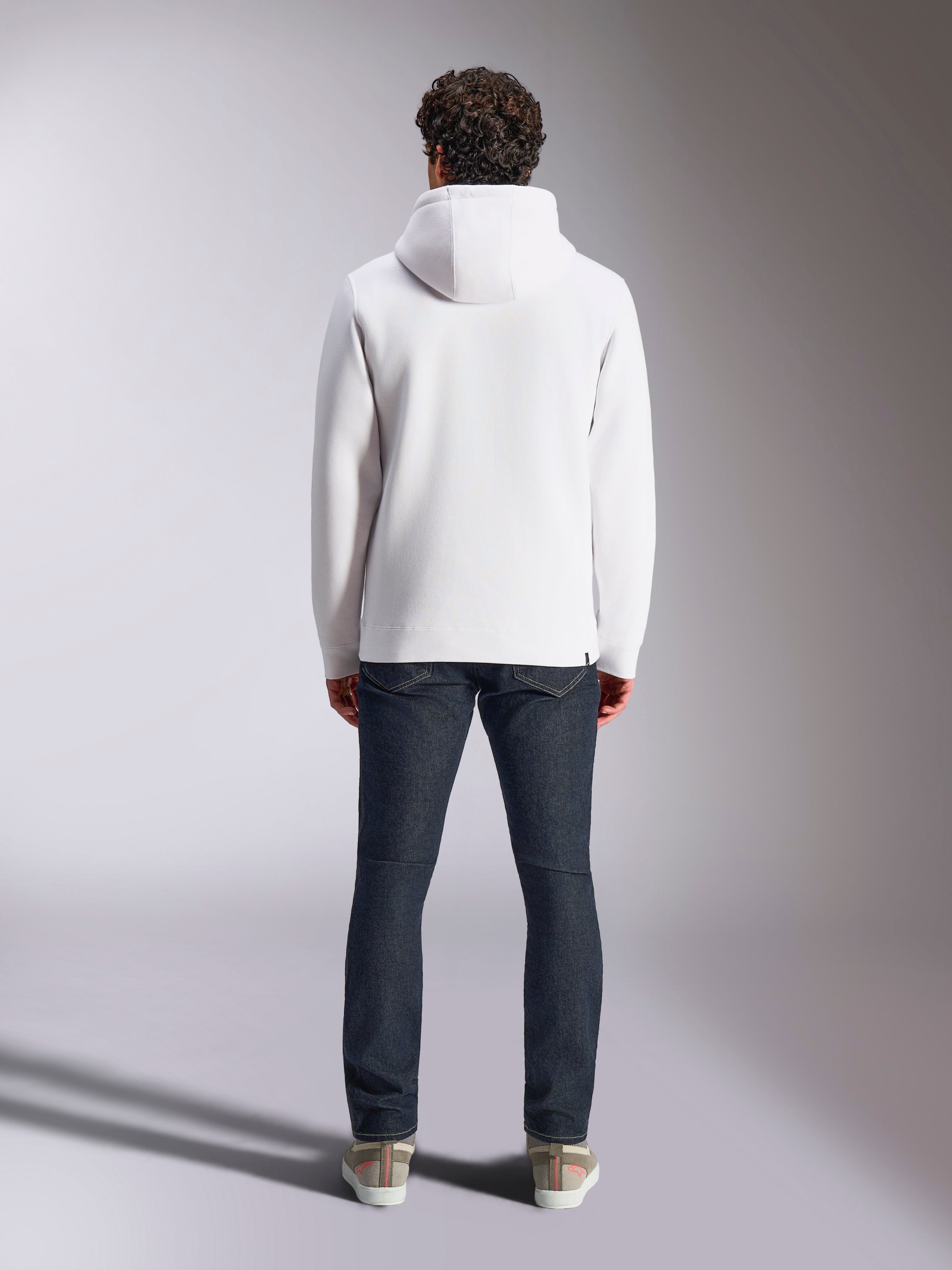Alpinestars Blaze V3 hættetrøje, hvid afslappet sportstøjs-hættetrøje, set bagfra, pullover i fleece, stilrent design med ribkanter ved manchetter og søm, stylet med mørkeblå jeans og sneakers, moderne motorsport-inspireret livsstilstøj