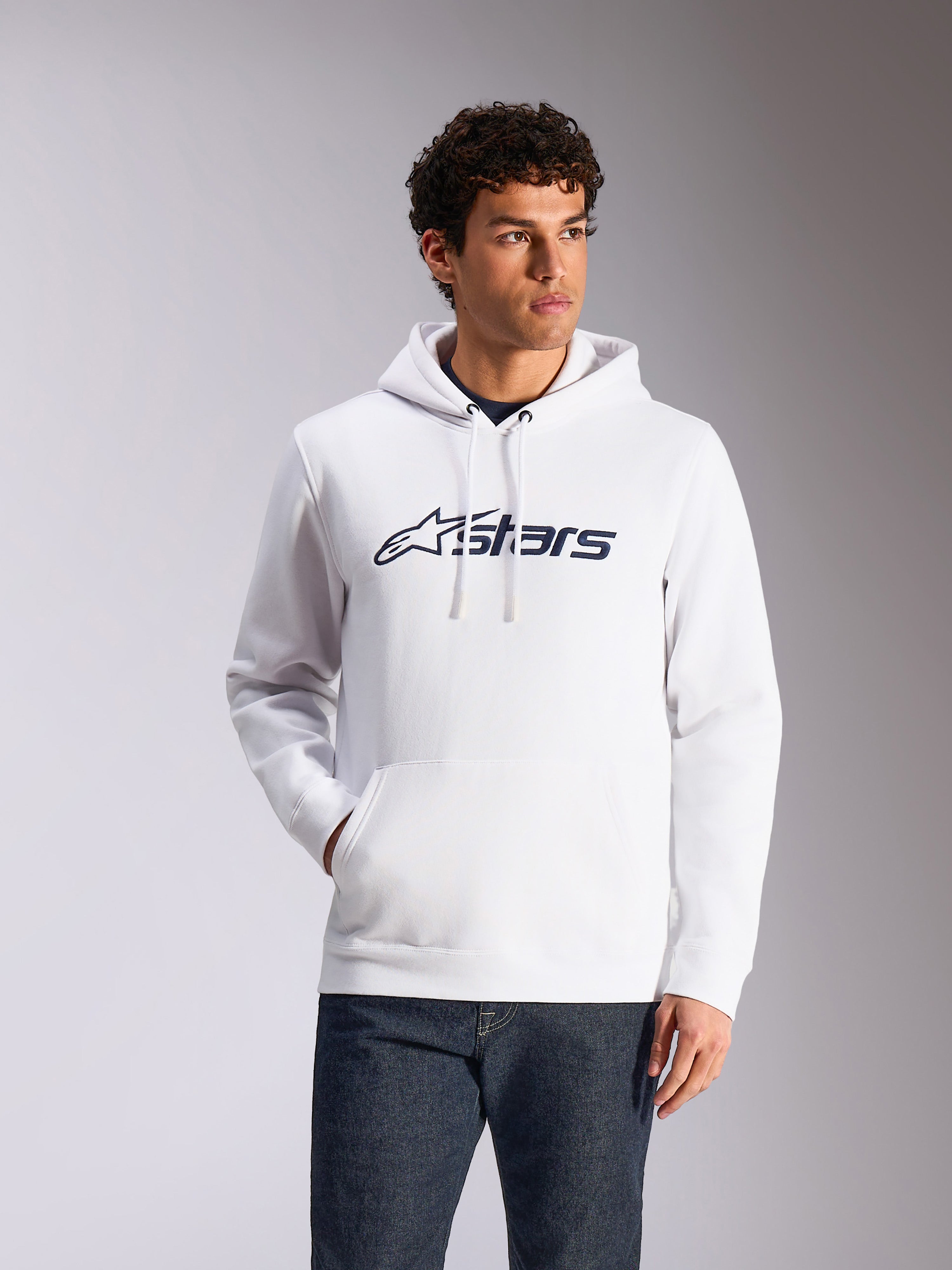 Alpinestars Blaze V3 Hoodie, afslappet streetwear, hvid med mørkeblåt Alpinestars-logo, hætte med snøre, lange ærmer, båret med mørke denimjeans, moderne motorsport-inspireret design