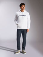 Alpinestars Blaze V3 hættetrøje, hvid afslappet streetwear-hættetrøje med mørkeblåt Alpinestars-logo på brystet, båret af en model med mørkeblå jeans og sandfarvede sneakers, med hætte med snoretræk og kængurulomme på fronten