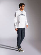 Alpinestars Blaze V3 hættetrøje, hvid og navy, afslappet streetwear båret af en model med mørkeblå jeans og sneakers, har hætte med snoretræk og markant logoprint på fronten, moderne motorsport-inspireret design