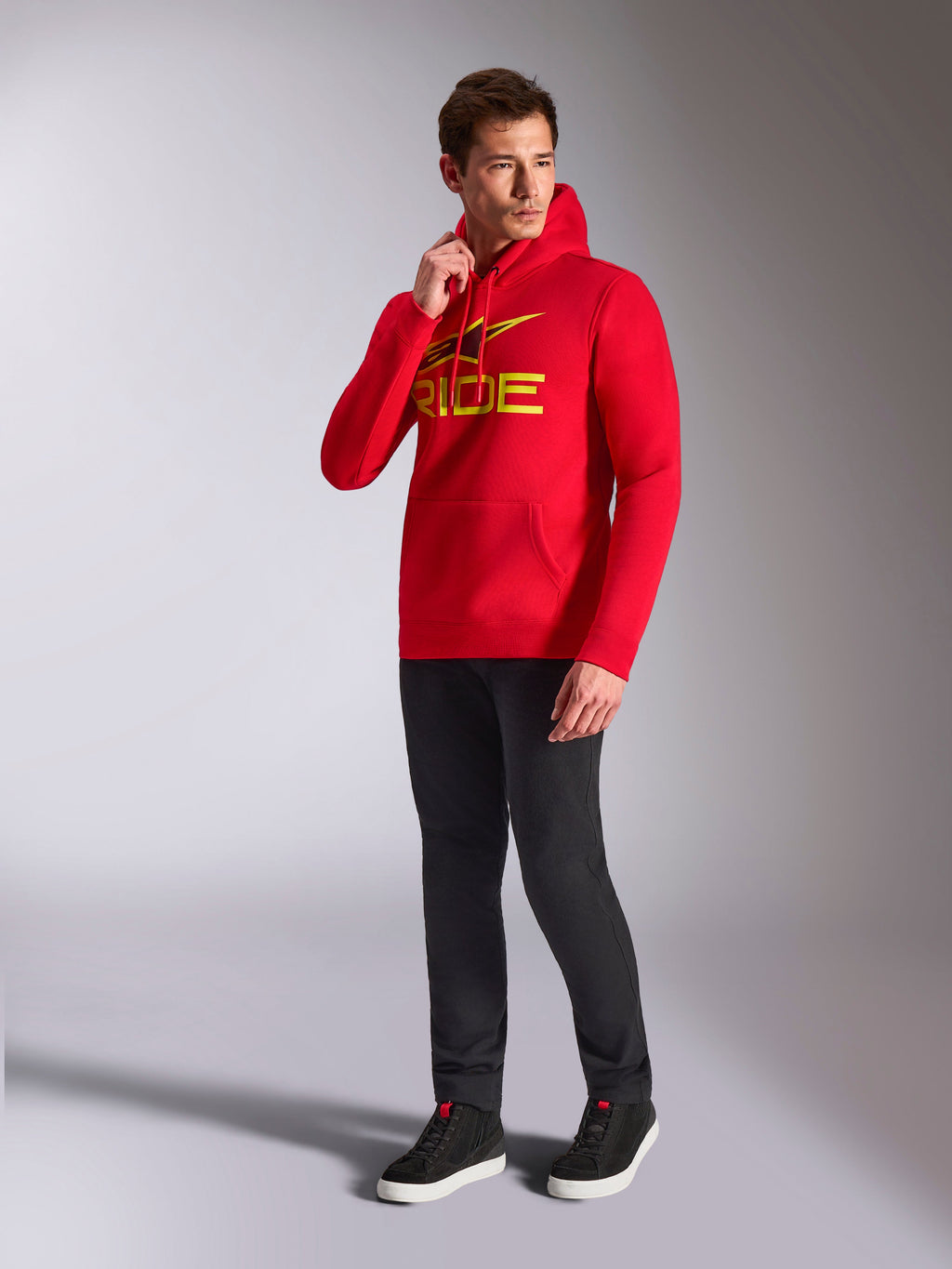 Alpinestars Ride V3 hættetrøje, rød pullover-sweatshirt, gult og sort 'RIDE'-logo på brystet, båret af model med sorte bukser og sorte sneakers, afslappet motorsport-inspireret streetwear