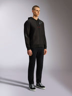 Alpinestars Sessions V3 hættetrøje, afslappet motorsport streetwear, sort hættetrøje med lynlås med gråt stjernelogo på brystet og ærmet, snoretræk med røde spidser, ribkanter på ærmer og bund, bæres af en model med sorte bukser og sneakers