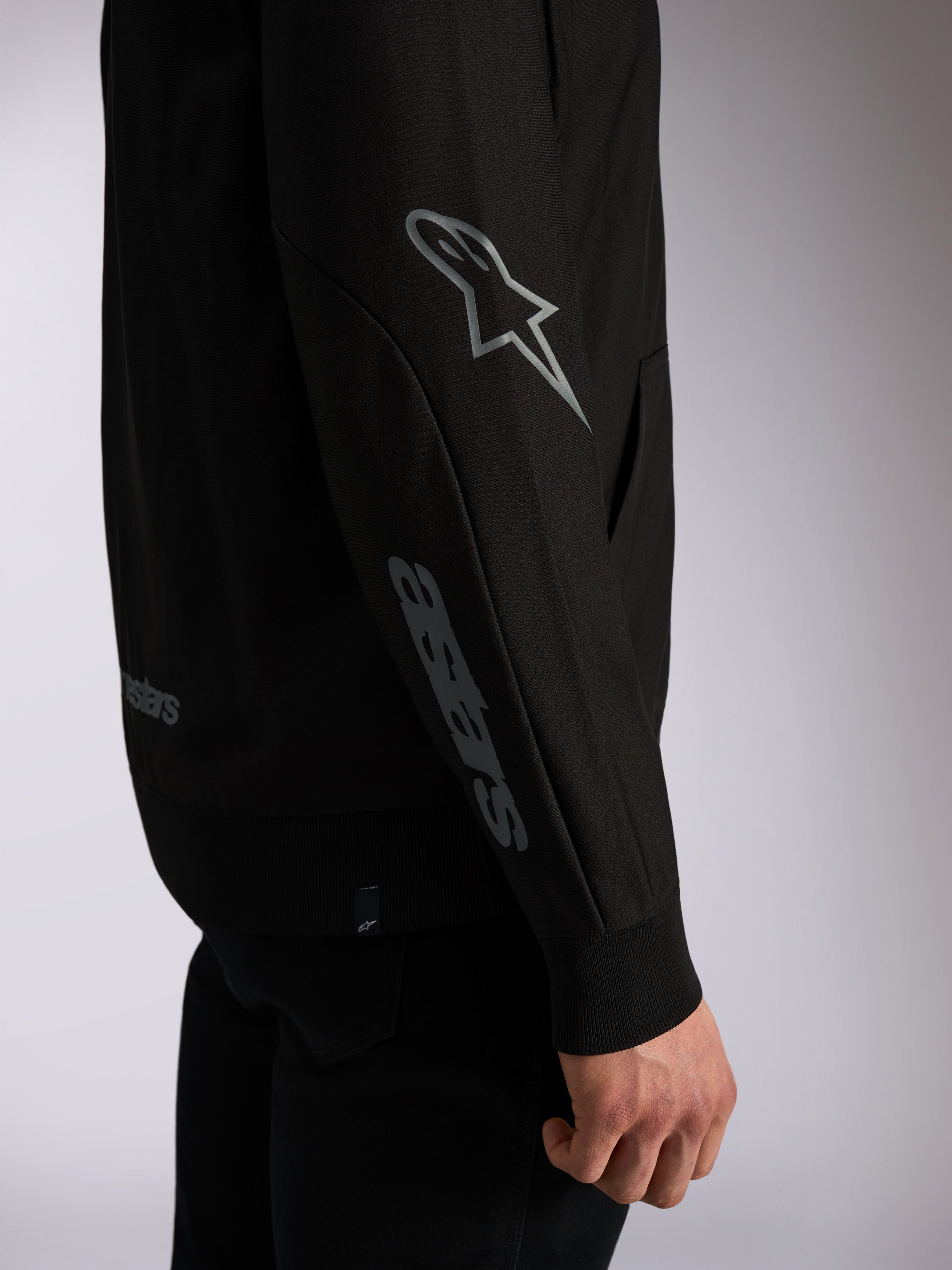 Alpinestars Sessions V3 hættetrøje, sort afslappet streetwear, nærbillede af ærme med gråt Astars-logo på albuen og ordmærke på underarmen, ribkanter, motorsport-inspireret design