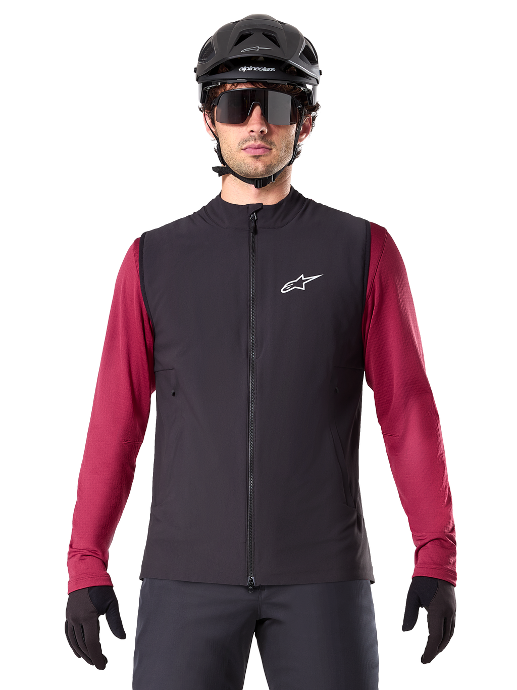 Alpinestars A-Dura Thermal Vest, sort isoleret cykelvest, båret af en model med en bordeauxrød langærmet trøje, sort MTB-hjelm og solbriller, hvidt logo på brystet, letvægts termisk beskyttelse til mountainbiking
