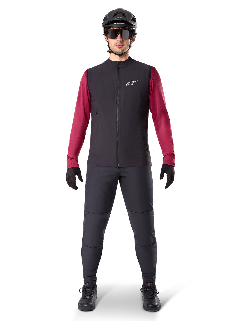 Alpinestars A-Dura Thermal Vest, sort cykelvest båret over en bordeauxfarvet langærmet trøje, kombineret med mørkegrå MTB-bukser, sort hjelm og solbriller, teknisk mountainbike-beklædning til kørsel i koldt vejr.