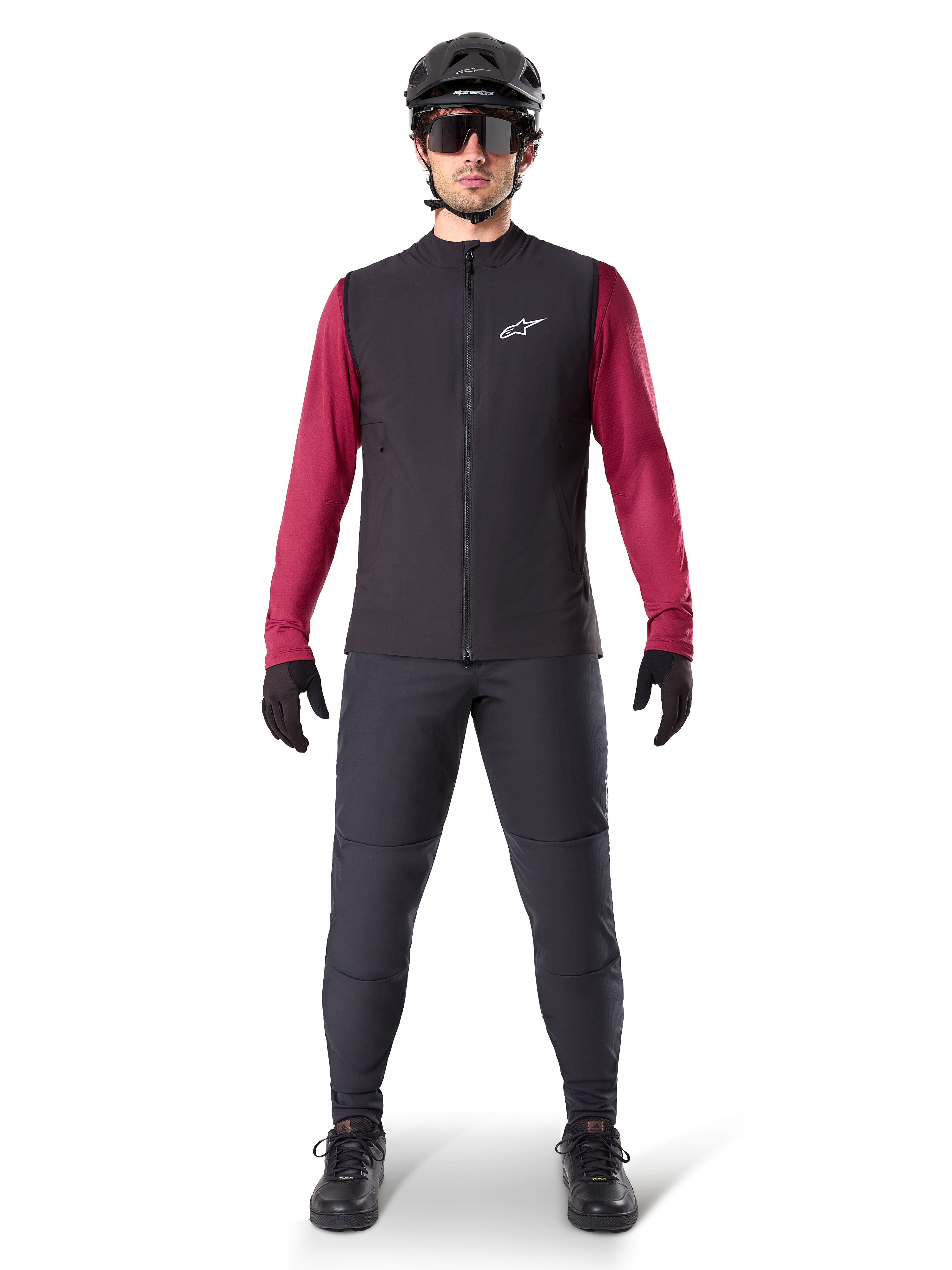 Alpinestars A-Dura Thermal Vest, sort cykelvest båret over en bordeauxfarvet langærmet trøje, kombineret med mørkegrå MTB-bukser, sort hjelm og solbriller, teknisk mountainbike-beklædning til kørsel i koldt vejr.