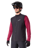 Alpinestars A-Dura Thermal Vest, sort termisk cykelvest, bæres over en vinrød langærmet trøje, med hvidt logo på brystet, kombineret med en sort MTB-hjelm og solbriller, isolerende præstationslag til mountainbiking