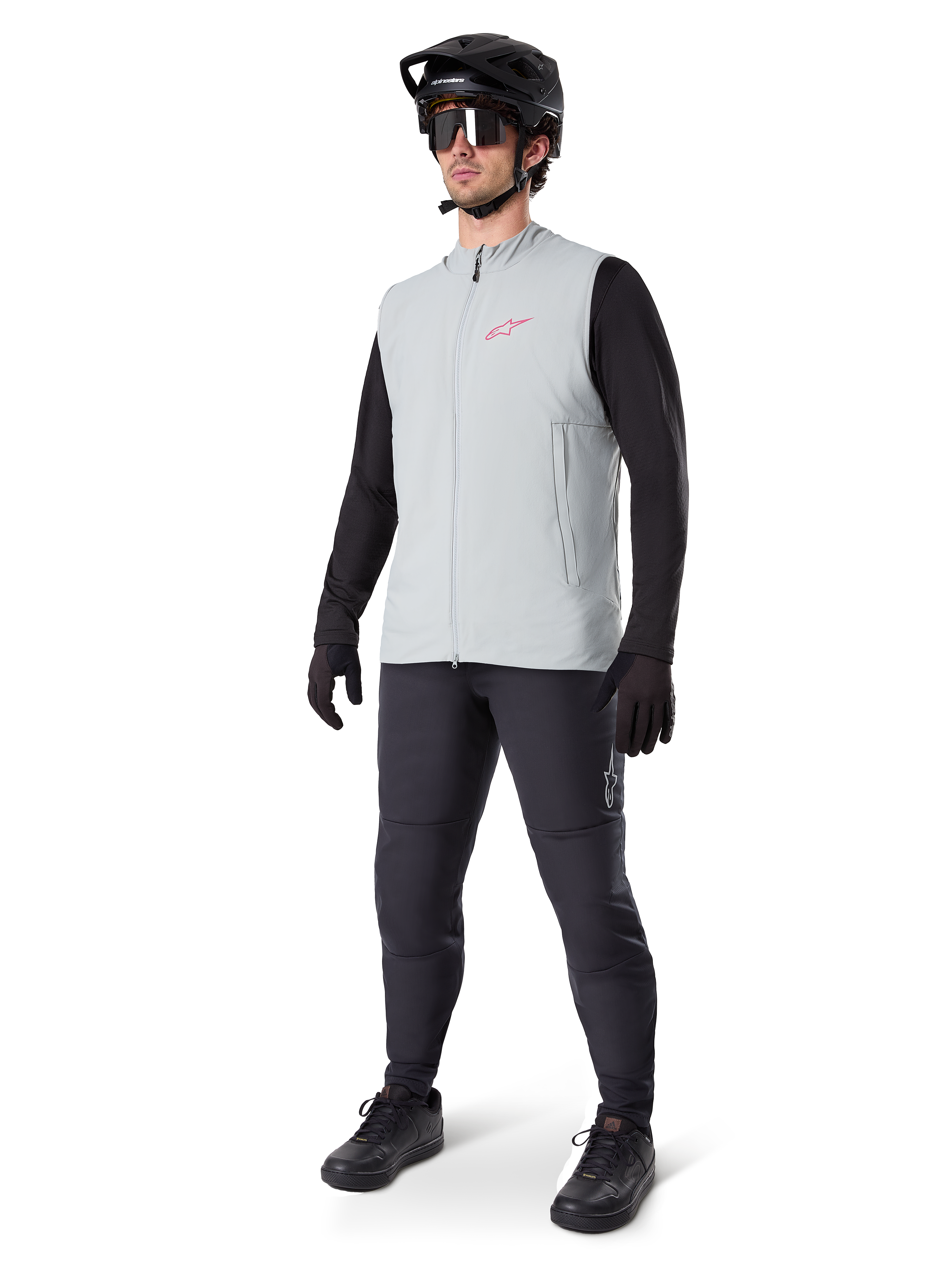 Alpinestars A-Dura termovest, titaniumgrå cykelvest med et lyserødt logo, båret af en model med en sort langærmet trøje, mørkegrå bukser og en sort mountainbikehjelm, performance-udstyr til kørsel i koldt vejr