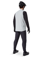Alpinestars A-Dura Thermal Vest, Titanium Gray, set bagfra af model iført den isolerede cykelvest over en sort langærmet trøje og mørke bukser, komplet med en sort mountainbikehjelm og handsker, designet til terrænkørsel i koldt vejr